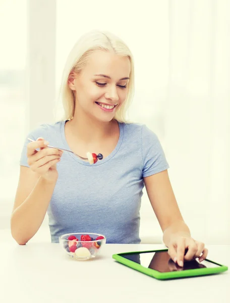 Smiling woman eating fruits with tablet pc at home — Stock Photo, Image