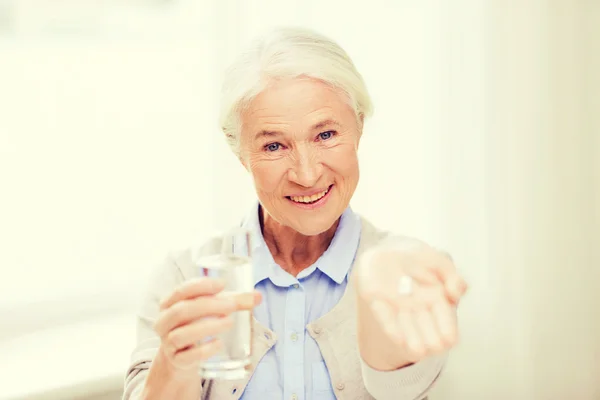 Ευτυχής ανώτερος γυναίκα με νερό και τα φάρμακα στο σπίτι — Φωτογραφία Αρχείου
