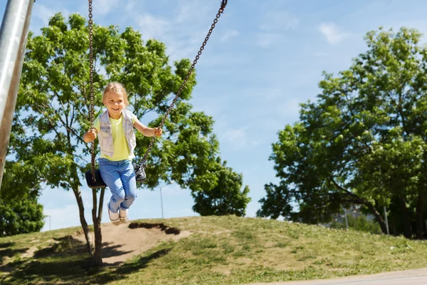 Fröhliches kleines Mädchen schaukelt auf Schaukel auf Spielplatz — Stockfoto