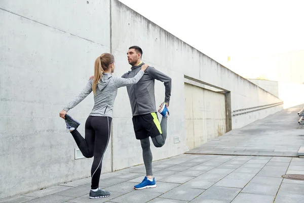 Couple of sportsmen stretching leg on city street — Stock Photo, Image