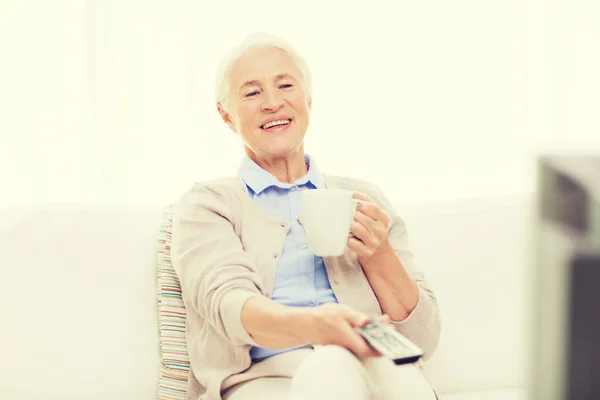 Senior woman watching tv and drinking tea at home — Stock Photo, Image