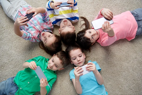 happy children with smartphones lying on floor