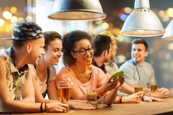 Amigos felizes com smartphone e bebidas no bar — Fotografia de Stock