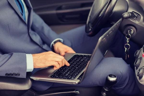 Close up of young man with laptop driving car — Stock Photo, Image