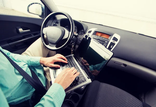 Close up of young man with laptop driving car — Stock Photo, Image