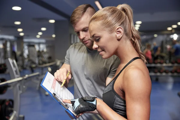 Femme souriante avec entraîneur et presse-papiers dans la salle de gym — Photo