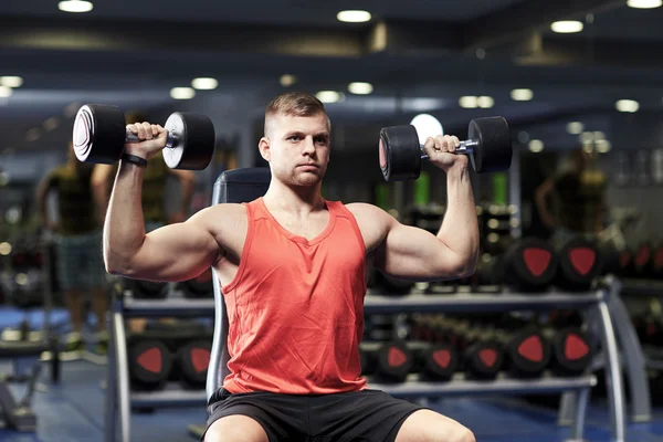 Junger Mann mit Hanteln lässt Muskeln im Fitnessstudio spielen — Stockfoto