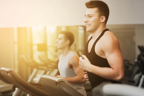 Lächelnde Männer beim Training auf dem Laufband im Fitnessstudio — Stockfoto