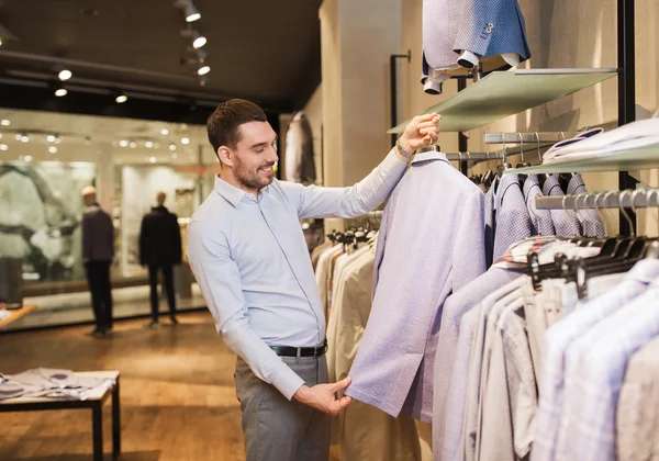 Счастливый молодой человек выбирает одежду в магазине одежды — стоковое фото