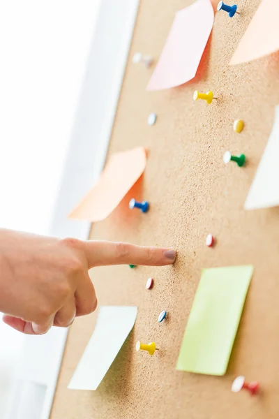 Hand pointing to cork board with stickers and pins — Stock Photo, Image