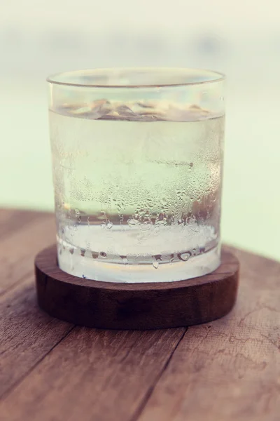Стакан воды с кубиками льда на столе на пляже — стоковое фото