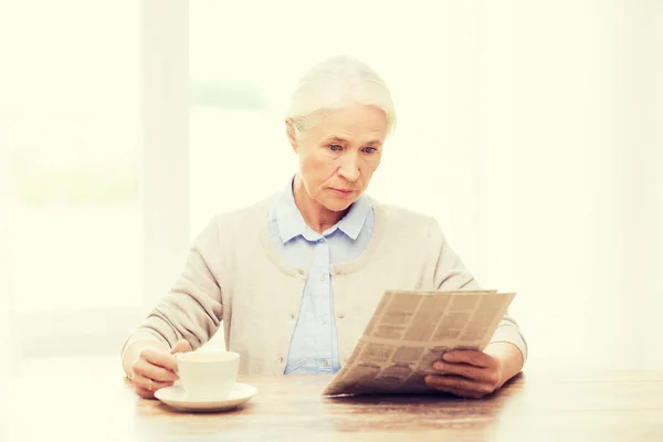 Пожилая женщина с газетой для чтения кофе дома — стоковое фото