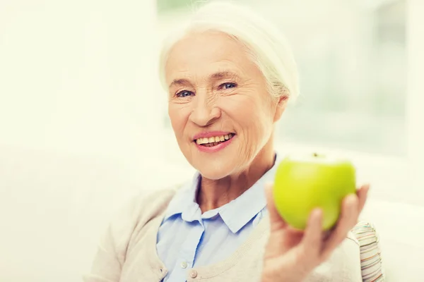 Glückliche Seniorin mit grünem Apfel zu Hause — Stockfoto