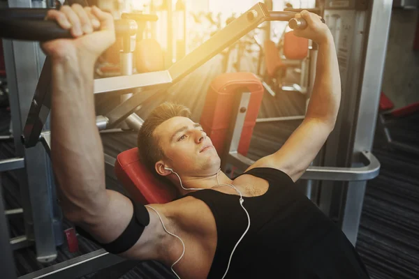 Young man with earphones exercising on gym machine — Stock Photo, Image