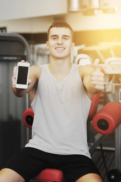 व्यायामशाळा मध्ये स्मार्टफोन तरुण माणूस हसत — स्टॉक फोटो, इमेज