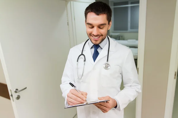 Happy doctor writing to clipboard at hospital — Stock Photo, Image