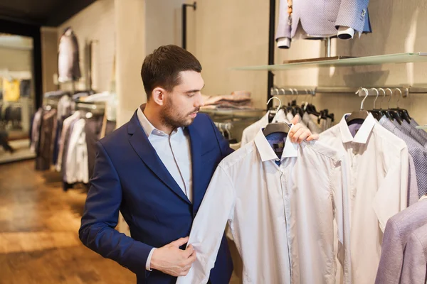 Happy young man choosing shirt in clothing store — Stock Photo, Image