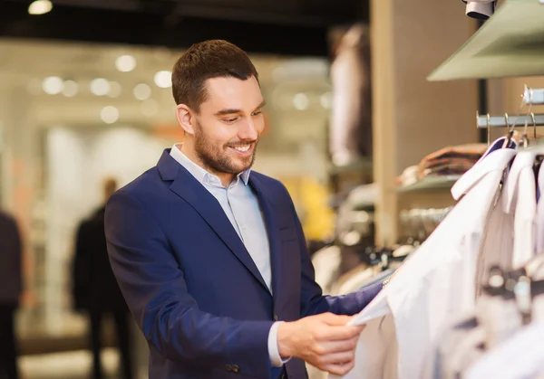 Happy young man choosing clothes in clothing store — Stock Photo, Image