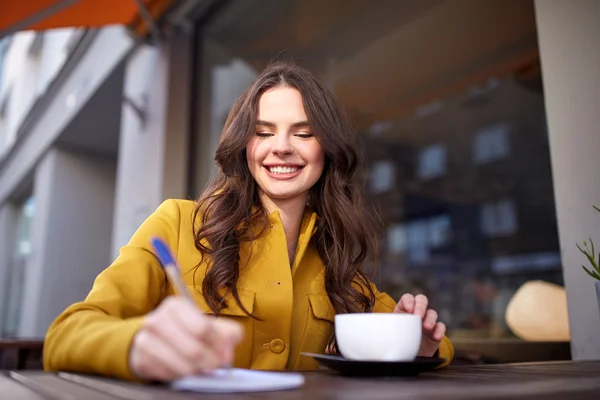 Glückliche Frau mit Notizbuch trinkt Kakao im Café — Stockfoto