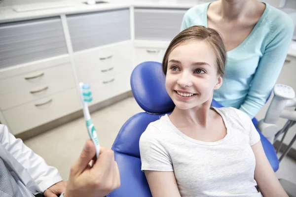 Dentista feliz mostrando cepillo de dientes a chica paciente — Foto de Stock