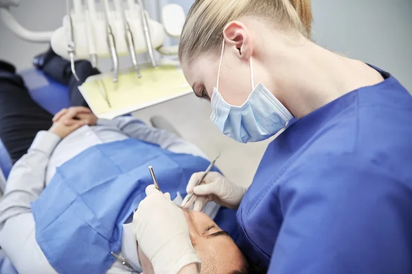 Dentista femenino en máscara chequeo de dientes de paciente masculino — Foto de Stock