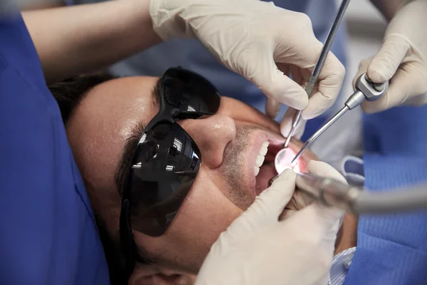Dentiste mains traitant les dents du patient masculin — Photo
