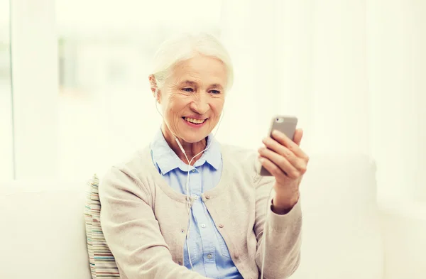 Äldre kvinna med smartphone och hörlurar hemma — Stockfoto