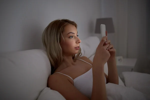 Jeune femme avec smartphone dans le lit à la maison chambre — Photo