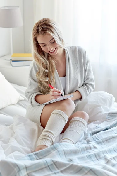 Glückliche junge Frau mit Notizbuch zu Hause im Bett — Stockfoto