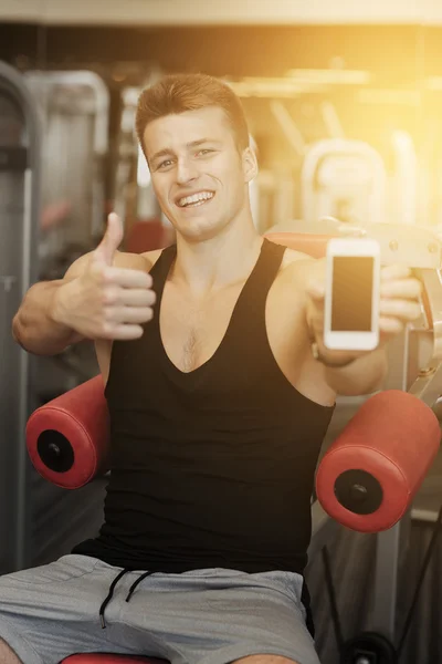 Улыбающийся молодой человек со смартфоном в тренажерном зале — стоковое фото