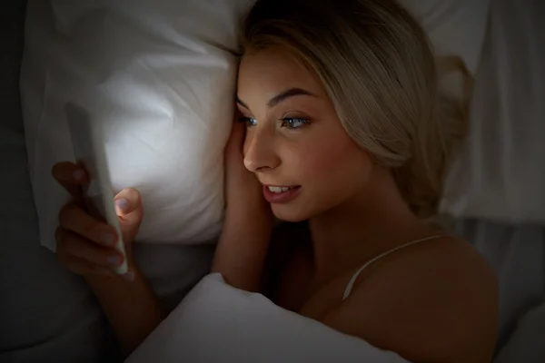 Jeune femme avec smartphone dans le lit à la maison chambre — Photo