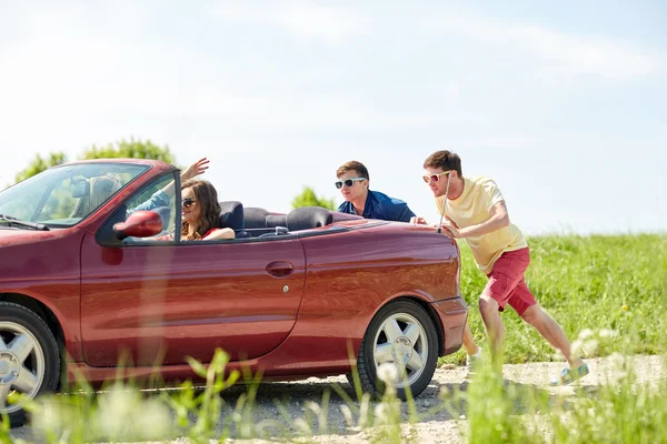 Amigos felices empujando coche cabriolet roto — Foto de Stock