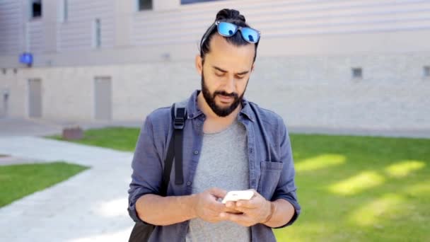 Hombre con mochila mensajes de texto en el teléfono inteligente en la ciudad — Vídeos de Stock