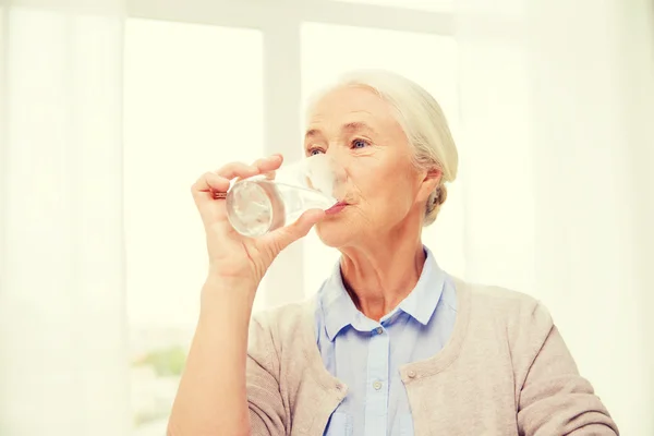 Счастливая пожилая женщина со стаканом воды дома — стоковое фото