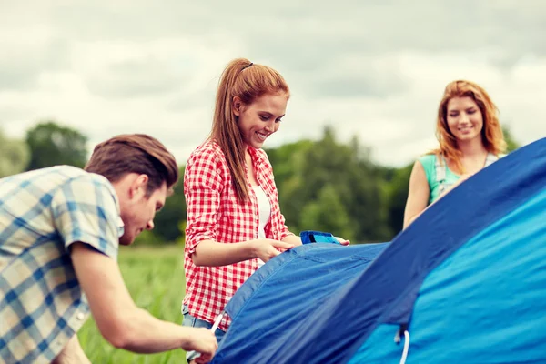 Grupo de amigos sorridentes montando tenda ao ar livre — Fotografia de Stock