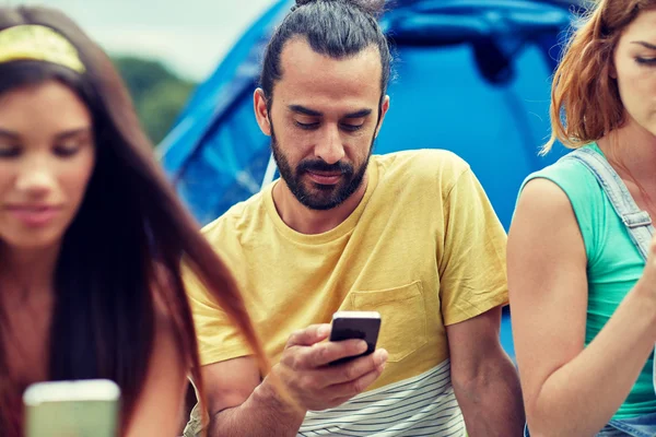 Amigos com smartphone e barraca no acampamento — Fotografia de Stock