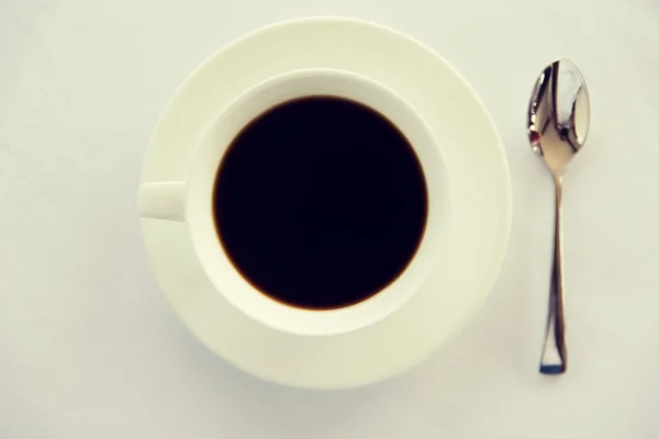 Kopje zwarte koffie met lepel en schotel op tafel — Stockfoto