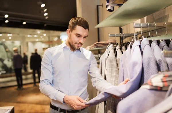 Gelukkig jonge man kiezen kleren in kledingwinkel — Stockfoto