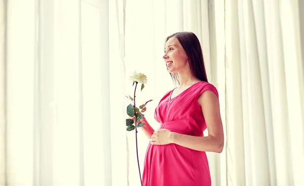 Mujer embarazada feliz con flor de rosa en casa — Foto de Stock