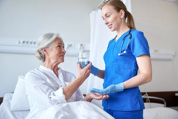 Enfermera que da medicina a una mujer mayor en el hospital — Foto de Stock