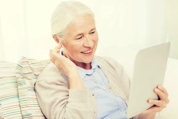 Donna anziana con tablet pc e auricolari a casa — Foto Stock