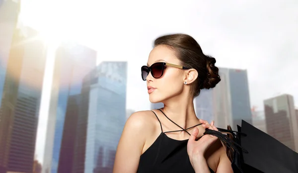 Gelukkige vrouw in zwarte zonnebril met shopping tassen — Stockfoto
