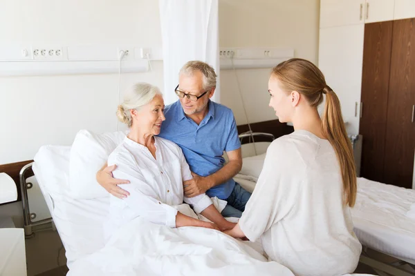 Familia feliz visitando a la mujer mayor en el hospital —  Fotos de Stock