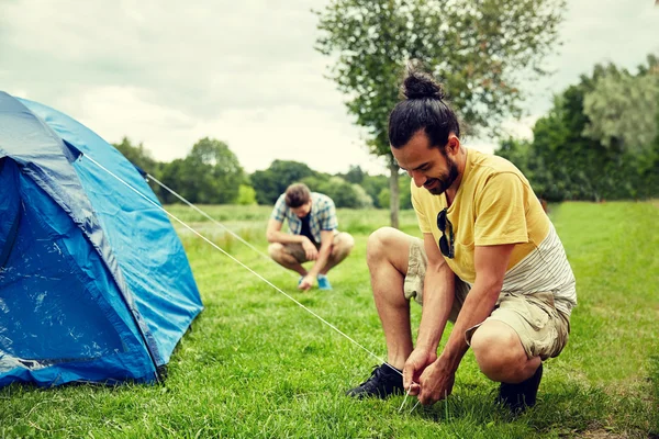 Amigos sorridentes montando tenda ao ar livre — Fotografia de Stock