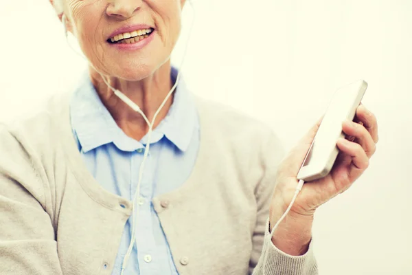 Счастливая пожилая женщина со смартфоном и наушниками — стоковое фото