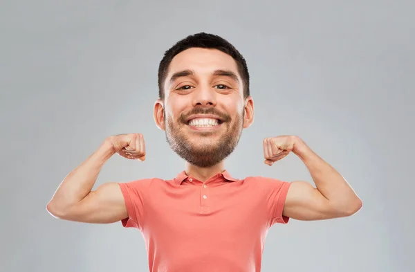 Usmívající se muž ukazuje biceps šedé pozadí — Stock fotografie