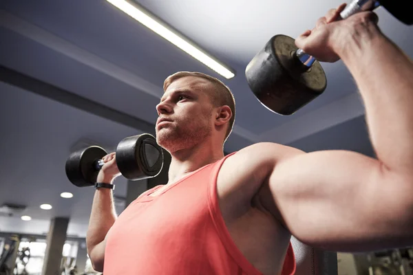 Young man with dumbbells flexing muscles in gym — Stock Photo, Image