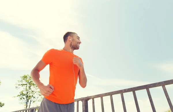 Happy man with earphones running outdoors — Stock Photo, Image