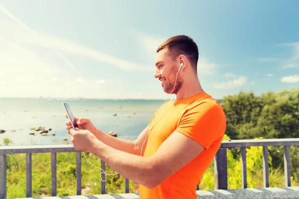 Joven sonriente con teléfono inteligente y auriculares — Foto de Stock