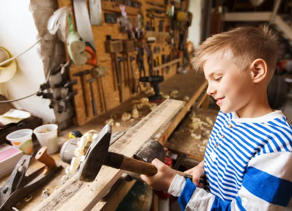 Glücklicher kleiner Junge mit Hammer und Planke in Werkstatt — Stockfoto